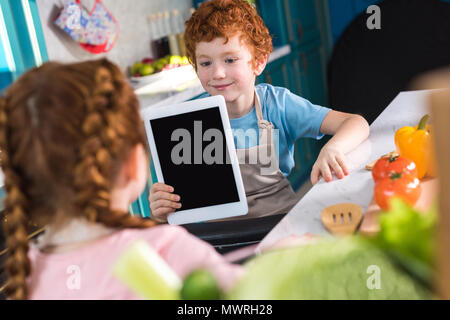 Adorabili bambini utilizzando tavoletta digitale mentre si cucina insieme in cucina Foto Stock