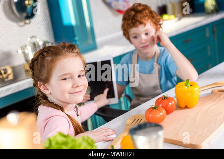 I bambini con tavoletta digitale mentre si cucina insieme in cucina Foto Stock