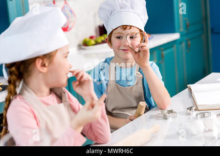 Adorabili bambini in chef cappelli e grembiuli sorridente ogni altro mentre la cucina insieme in cucina Foto Stock