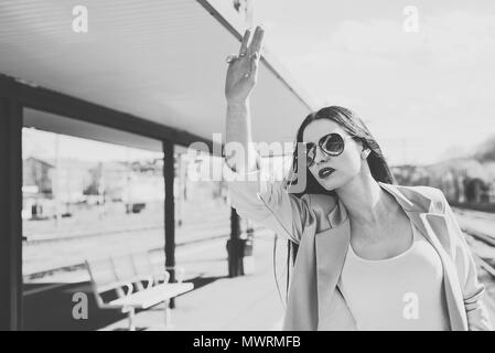 Vintage guardare una donna che chiama gli amici. La donna sulla piattaforma solleva la sua mano chiamando qualcuno. Una bella e attraente donna indossa sungla Foto Stock