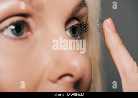 Vista ravvicinata della donna l'applicazione di lenti a contatto isolato su grigio Foto Stock