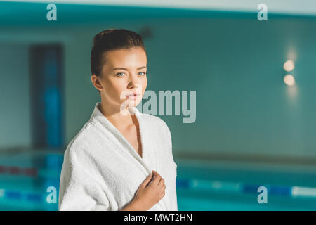 Bella giovane donna in accappatoio davanti alla piscina spa Foto Stock