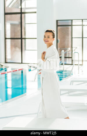 Bella giovane donna in accappatoio in piedi accanto alla piscina presso il salone di spa Foto Stock