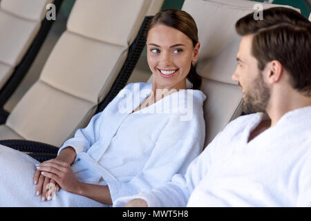 Felice coppia giovane in accappatoi sorridente ogni altro durante il riposo insieme nel centro spa Foto Stock