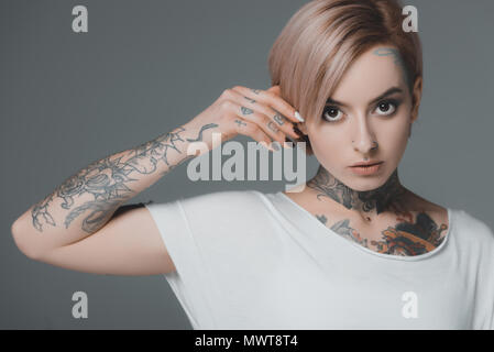 Ritratto di giovane e bella donna con tatuaggi guardando la telecamera isolato su grigio Foto Stock