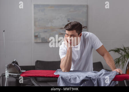 Uomo bello in appoggio il mento sulla mano e guardando lontano nel soggiorno Foto Stock