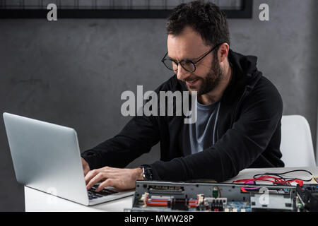 Uomo sorridente con notebook contro rotture di pc sul tavolo Foto Stock