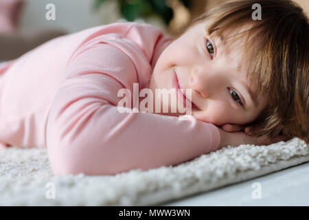 Bambino sorridente ragazza con la sindrome di down sdraiato sul pavimento morbido tappeto Foto Stock