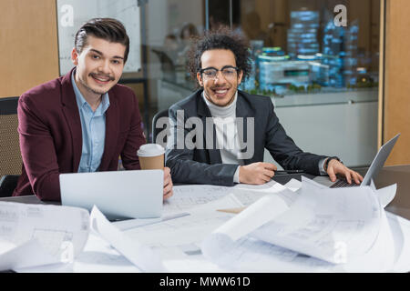 Felice giovani architetti con piani di costruzione seduti insieme a office Foto Stock