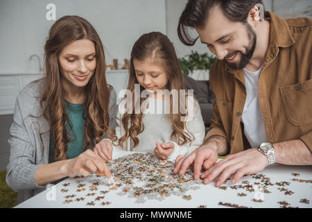 Genitori felici e la figlia il collegamento di pezzi di un puzzle a tavola Foto Stock