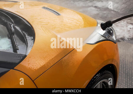 Giallo auto anteriore lavata con acqua a spruzzo a getto in autolavaggi. Foto Stock