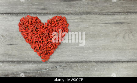 Vista superiore a forma di cuore simbolo fatta di goji (wolfberry) Bacche di colore grigio sulla scrivania di legno Foto Stock