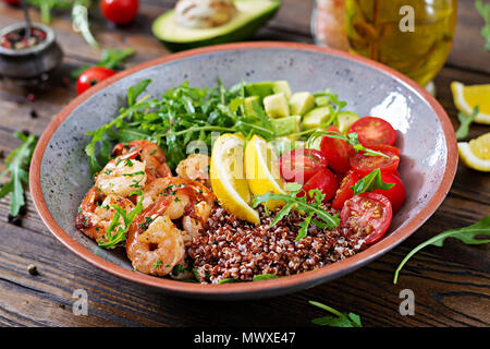 Deliziosi Buddha sani ciotola con gamberetti, pomodoro, avocado, quinoa, succo di limone e foglie di rucola sul tavolo di legno. Cibo sano. Foto Stock