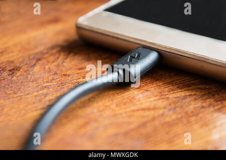 La spina del caricabatterie al telefono sul tavolo di legno sfondo Foto Stock