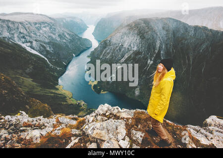 Donna traveler sulla scogliera di montagna in piedi da solo in viaggio in Norvegia Lifestyle Vacanze avventura aerea vista del fiordo bambina indossa un impermeabile giallo walki Foto Stock