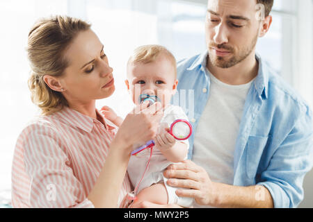 Giovane madre dando manichino bambino alla figlia infante mentre padre toccando il suo Foto Stock