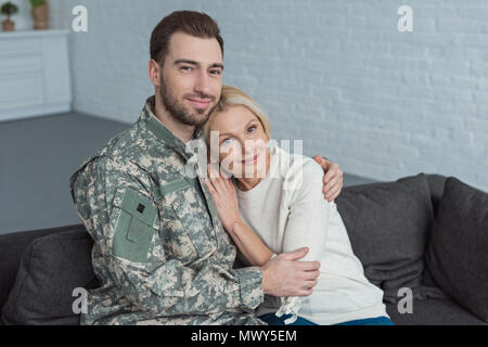 Ritratto di uomo in uniforme militare abbracciando sorridente madre sul divano di casa Foto Stock
