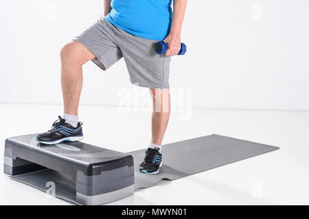 Vista parziale di senior uomo con manubri esercizio sullo stepper isolato su grigio Foto Stock