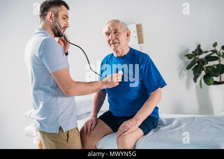 Terapista della riabilitazione con uno stetoscopio controllo senior mans heartbeat Foto Stock