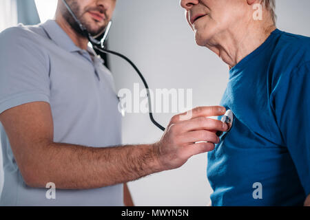 Ritagliato shot del terapista della riabilitazione con uno stetoscopio controllo senior mans heartbeat Foto Stock