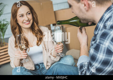 Ritagliato shot dell'uomo versando champagne in bicchieri mentre sorridente moglie seduta vicino le scatole di cartone Foto Stock