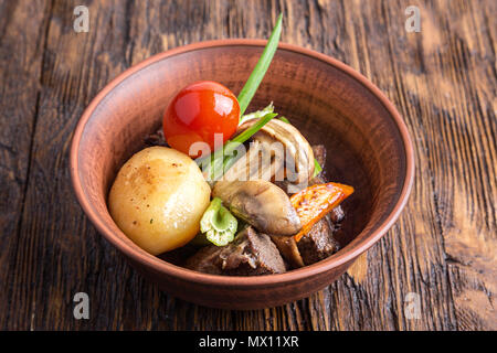 Stufato di carne con verdure in un tegame di coccio. funghi, carote, pomodori, sedano, cipolla. orizzontale Foto Stock