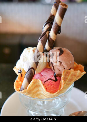 Mescolati ice cream scoop nella ciotola del wafer. Gelato Dessert napoletano con gusti di gelato - piatto di vetro con palline di cioccolato, la vaniglia e il gelato alla fragola con laminati biscotti Cookie e condimenti Foto Stock