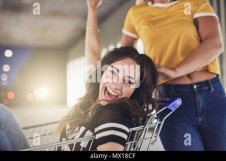 Ridendo giovane donna essendo spinto in un carrello da due amici nella città di notte Foto Stock