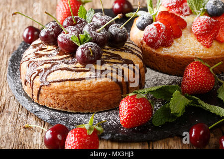 Torte dessert con cioccolato, menta, fragole, ciliegie e mirtilli vicino sul tavolo orizzontale. Foto Stock