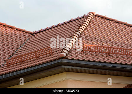 Close-up dettaglio del tetto incastrata con neve e ghiaccio recinto di protezione e sul nuovo grande casa moderna con tegole rosse contro il cielo blu sullo sfondo. P Foto Stock