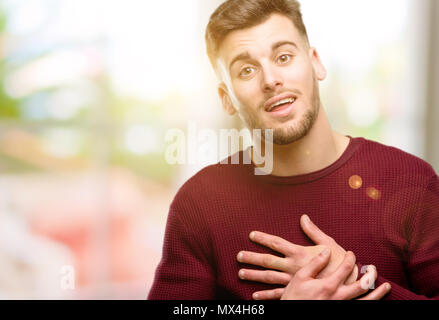 Bel giovane avente affascinante sorriso tenendo le mani sul cuore che vogliono mostrare amore e simpatia Foto Stock