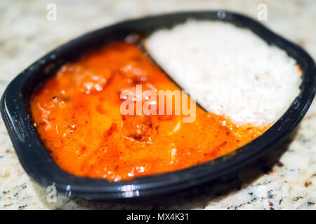 Macro closeup di rosso arancione curry tikka masala salsa in plastica nera cena tv fast food pasto congelato il contenitore sulla tabella con il bianco di riso basmati Foto Stock