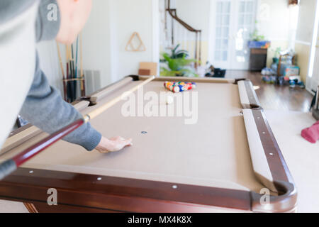 Interno all'interno di casa home con il biliardo tavolo da biliardo in soggiorno, uomo nel freddo inverno maglione riprese la sfera bianca durante il gioco avvia con cue Foto Stock