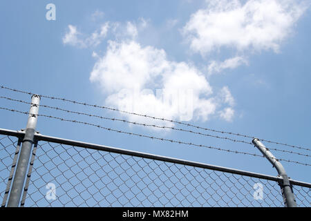 Rete di recinzione a maglie con filo spinato su uno sfondo di cielo blu Foto Stock