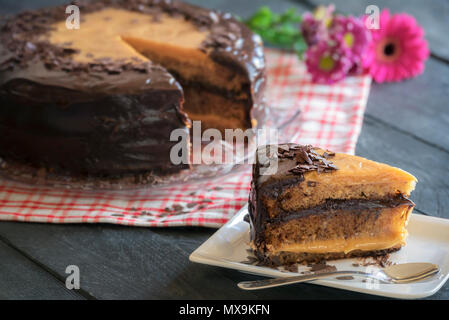 Gustoso pezzo di torta con un riempimento Brigadeiro fatta con il latte condensato e cioccolato, con tutta la torta in background su un rustico tavolo indietro. Foto Stock