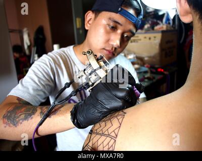 MANDALUYONG City, Filippine - 27 Maggio 2018: Un tatuaggio artista lavora su un tatuaggio sulla spalla di un cliente. Foto Stock