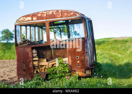 Close-up del vecchio abbandonato bus passeggero con le finestre rotte ruggine in alta verde erba con erbacce sul bordo di arata brown field sulla luminosa giornata di primavera sotto Foto Stock