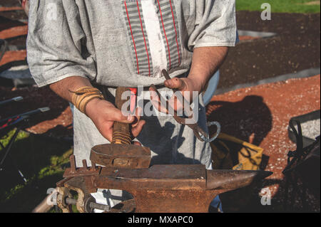 Le mani di un fabbro forgiare le parti di metallo sulla vecchia incudine su un fuoco aperto. Artigianato popolare Foto Stock