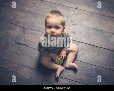 Un piccolo bambino seduto sul floorboardswith un Apple ed è la ricerca di Foto Stock