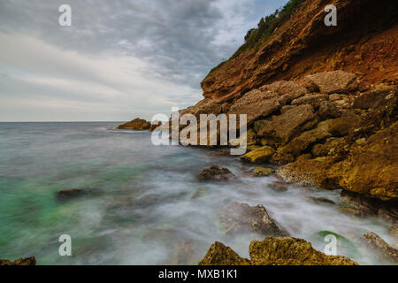 Tramonto sulla spiaggia tra le rocce vicino alla città di Denia. Distretto di Valencia, Spagna. Foto Stock