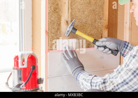 Il lavoratore fa opere di finitura delle pareti con un bianco tavola di legno, utilizzando una linea laser livello. Costruzione di isolante termico eco-telaio in legno casa con legno piastre in fibra Foto Stock