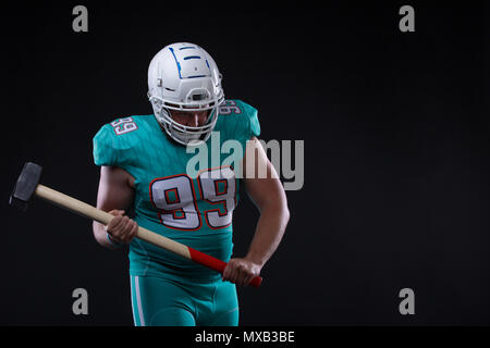 Aggressiva di giocatore di football americano in maglia blu urlando contro lo sfondo nero. giocatore di rugby tenendo un martello. Spazio di copia Foto Stock