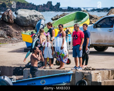 Uomo in wetsuit chiamando fuori dalla piccola barca in porto con la popolazione locale sulla banchina, Hanga Roa, Isola di Pasqua, Cile Foto Stock