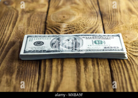 Un pacco di banconote da cento dollari su un tavolo di legno. Piccole profondità di campo. Focus sul Presidente Franklin. Foto Stock