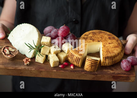 Un vassoio di formaggi con formaggi assortiti, uva, dadi nelle mani del casaro. Formaggi italiani e piatti di frutta. Foto Stock