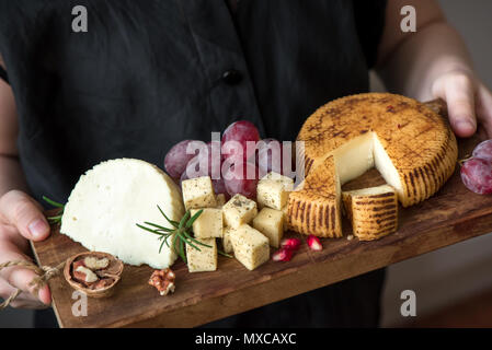 Un vassoio di formaggi con formaggi assortiti, uva, dadi nelle mani del casaro. Formaggi italiani e piatti di frutta. Foto Stock
