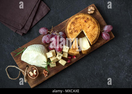 Un vassoio di formaggi con formaggi assortiti, uva, i dadi su sfondo nero, copia dello spazio. Formaggi italiani e piatti di frutta. Foto Stock