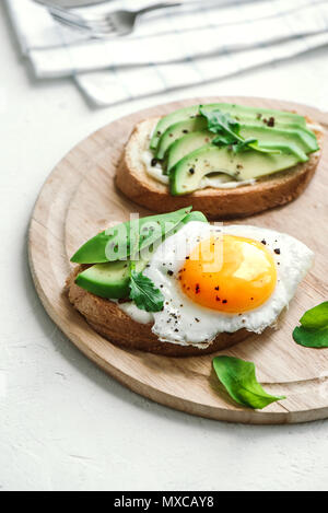 Sandwich di Avocado con uovo fritto - fette di avocado e uovo su pane tostato per una sana prima colazione o uno spuntino, copia dello spazio. Foto Stock