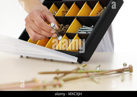 Lavoratore a mano scegli un dado viti dalla scatola, close up Foto Stock