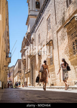 Due donne a piedi lungo una strada stretta in Mdina, antica città capitale di Malta, sotto il cielo limpido. Foto Stock